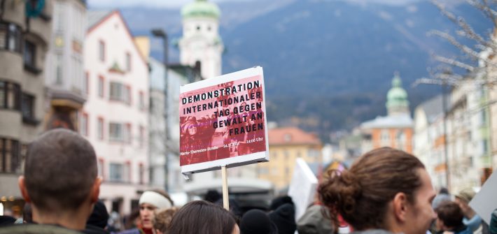 Demoschild mit der Aufschrift: Demonstration Internationaler Tag gegen Gewalt an Frauen. Im Hintergrund die Nordkette und Marien-Theresienstraße.